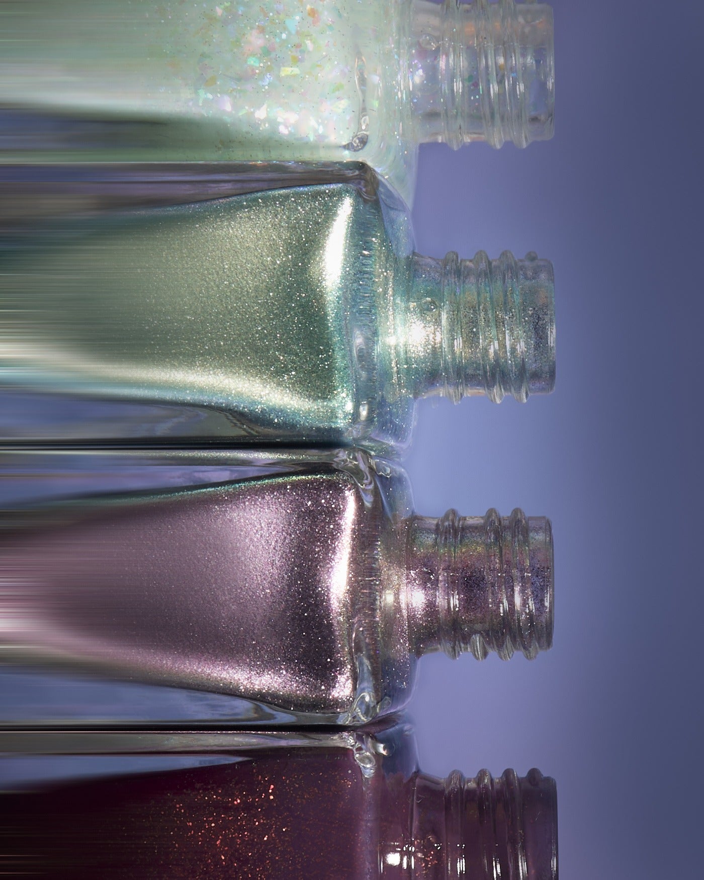 Band Of Misfits II Set: row of clear glass nail polish bottles with shimmering metallic glitter shades from iridescent green to deep purple